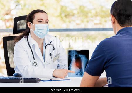 Aufnahme einer jungen Ärztin mit einer digitalen Tablette während einer Konsultation mit einem reifen Mann, der an langer Krankheit leidet Stockfoto