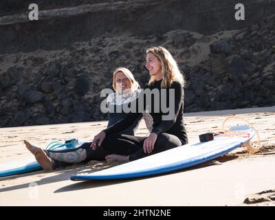 2 glückliche kaukasische Surfer sitzen am Strand. Sie lächeln und genießen das Leben. Freundschaft, gesundes Lifestyle-Konzept Stockfoto