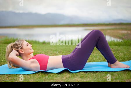 Hält ihre Kernmuskeln stark. Aufnahme einer jungen Frau, die im Freien Sit-ups macht. Stockfoto