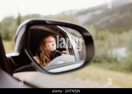 Kanada, Yukon, Whitehorse, lächelnde Frau mit Kamera im Autospiegel Stockfoto