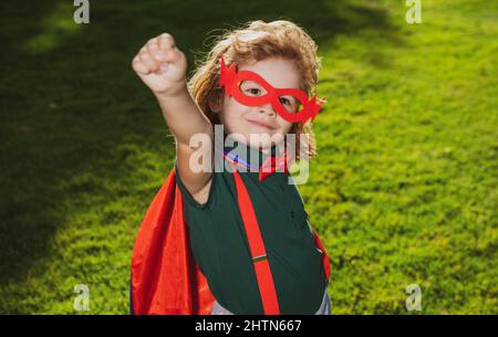 Tapferer Junge in einem Superhelden-Kostüm, mit rotem Cape und Maske, streckt seine Hand aus. Niedliches Kind spielt Superheld. Das Konzept von Macht und Gerechtigkeit. Stockfoto