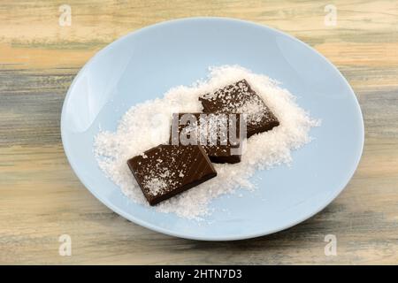 Dunkle Schokolade Bonbon Bar quadratische Stücke mit Meersalz auf blauen Snack-Teller Stockfoto