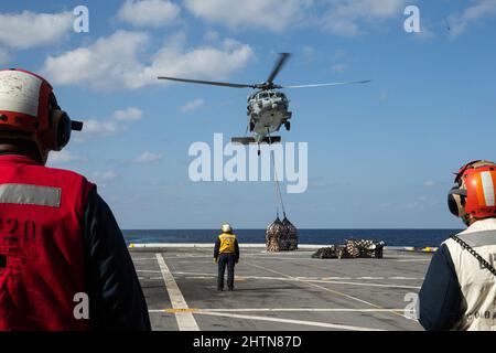 Seeleute der US-Marine beobachten während einer Nachversorgung auf See an Bord der USS Green Bay, Philippine Sea, 15. Februar 2022, eine MH-60s Sea Hawk, die Vorräte auf der Fluglinie anlandet. Die 31. MEU ist an Bord der Schiffe der America Amphibious Ready Group im Einsatzgebiet der 7. Flotten tätig, um die Interoperabilität mit Verbündeten und Partnern zu verbessern und als eine ready Reaktion zur Verteidigung von Frieden und Stabilität in der Indo-Pazifik-Region zu dienen. (USA Marine Corps Foto von Lance CPL. Yvonne Iwae) Stockfoto