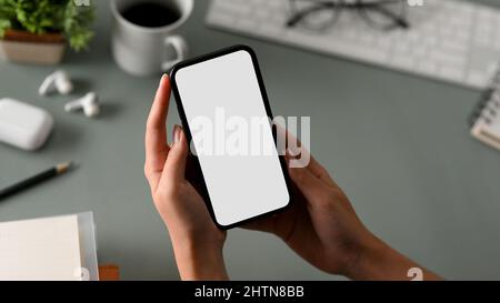 Ausgeschnittene Nahaufnahme einer Frau mit leerem Bildschirm und Smartphone in dunklem Büroarbeitsplatz. Stockfoto