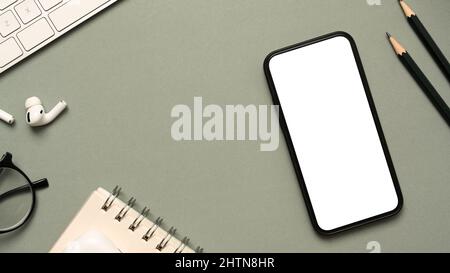 Büroarbeitstisch mit Office Essential Tools, Spiralnotepad, Ohrstöpsel, Brillen, Bleistift, Tastaturcomputer und Smartphone-Modell auf grauem Hintergrund Stockfoto