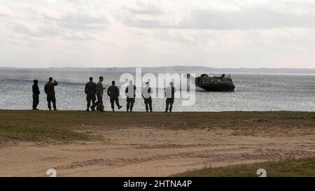 US-Marinesoldaten und Matrosen der Marine beobachten, wie ein Landungsschiff, Luftkissen mit Naval Beach Unit, während einer Abladung in Kin Blue, Okinawa, Japan, am 6. Februar 2022, in Richtung Küste fliegt. Die 31. MEU ist an Bord der Schiffe der America Amphibious Ready Group im Einsatzgebiet der 7. Flotten tätig, um die Interoperabilität mit Verbündeten und Partnern zu verbessern und als einsatzbereite Einsatztruppe zur Verteidigung von Frieden und Stabilität in der Indo-Pazifik-Region zu dienen. (USA Marine Corps Foto von Sgt. Danny Gonzalez) Stockfoto