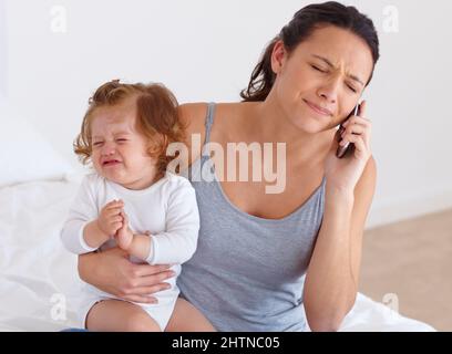 Der Versuch, alles auszugleichen - Mutterschaft. Eine Mutter, die versucht, ein Telefongespräch zu führen, während ihr Baby im Hintergrund weint. Stockfoto