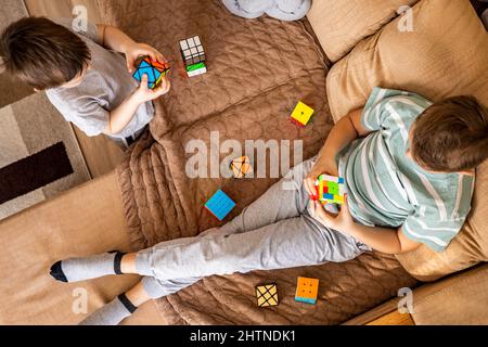 Draufsicht zwei Teenager- und Baby-Brüder, die bunte Rubik-Würfel auf der Couch zusammenbauen Stockfoto
