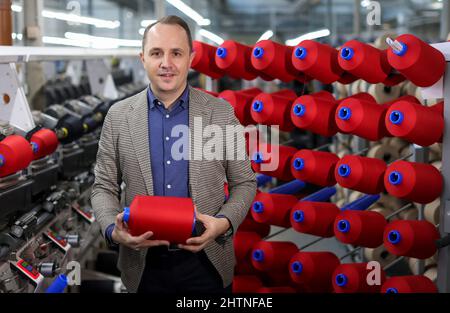 01. März 2022, Sachsen, Flöha: Nico Teutsch, Geschäftsführer, steht im Wickelraum der OTEX Textilveredlung GmbH. Das Unternehmen mit 90 Mitarbeitern stellt Spezialgarne für Medizinprodukte und technische Textilien her. Als 2016 nach einem Nachfolger für das Werk gesucht wurde, übernahm die Thüringer Bauerfeind AG, Hersteller von medizinischen Hilfsmitteln wie Verbänden, Orthesen oder orthopädischen Einlagen, einfach ihren Lieferanten selbst. Die Zahl der Beschäftigten stieg, und nun gehören auch mehrere Rumänen und Südamerikaner zur Belegschaft. Am Mittwoch (02.03.2022), die Vereinigung der Ost-Ge Stockfoto