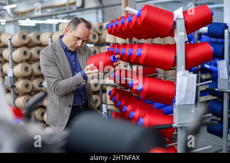 01. März 2022, Sachsen, Flöha: Nico Teutsch, Geschäftsführer, kontrolliert Garne in der Wickelabteilung der OTEX Textilveredlung GmbH. Das Unternehmen mit 90 Mitarbeitern produziert Spezialgarne für Medizinprodukte und technische Textilien. Bei der Suche nach einem Nachfolger für das Werk im Jahr 2016 übernahm die Thüringer Bauerfeind AG, ein Hersteller von medizinischen Hilfsmitteln wie Verbänden, Orthesen oder orthopädischen Einlagen, einfach den Lieferanten selbst. Die Zahl der Beschäftigten stieg, und nun gehören auch mehrere Rumänen und Südamerikaner zur Belegschaft. Am Mittwoch (02.03.2022), der Verband der Stockfoto