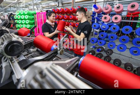 01. März 2022, Sachsen, Flöha: Zwei Mitarbeiter wechseln in der Wickelabteilung der OTEX Textilveredlung GmbH die Spulen mit farbigem Garn. Das Unternehmen mit 90 Mitarbeitern stellt Spezialgarne für Medizinprodukte und technische Textilien her. Als 2016 nach einem Nachfolger für das Werk gesucht wurde, übernahm die Thüringer Bauerfeind AG, Hersteller von medizinischen Hilfsmitteln wie Verbänden, Orthesen oder orthopädischen Einlagen, einfach ihren Lieferanten selbst. Die Zahl der Beschäftigten stieg, und nun gehören auch mehrere Rumänen und Südamerikaner zur Belegschaft. Am Mittwoch (02.03.2022), der Verein o Stockfoto