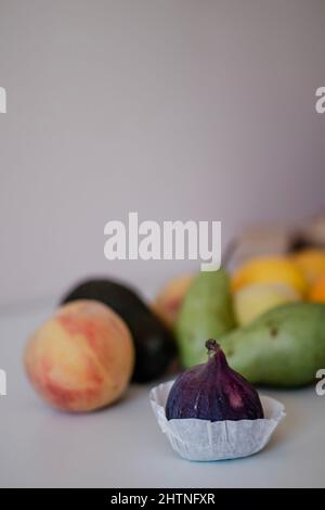Frische Feige im Vordergrund mit anderen Früchten auf hellem Hintergrund auf dem Tisch Stockfoto
