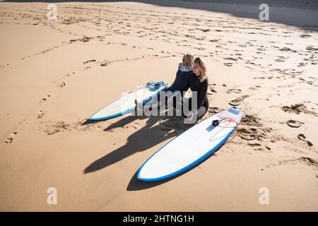 2 Surfer junge Frauen sitzen am Strand und beobachten die Wellen Stockfoto