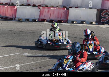 Blick auf drei Männer im Helm, die tagsüber Go-Kart auf der Kartbahn fahren Stockfoto