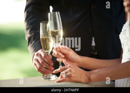 Bereit, ihre Liebe zu feiern. Beschnittene Ansicht einer jungen Braut und eines Bräutigams, die zusammen stehen und ihre Ehe toasten. Stockfoto