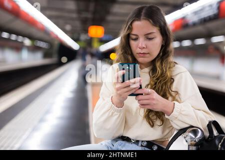 Junge attraktive Mädchen in Jeans warten auf U-Bahn-Zug auf einem Bahnsteig Stockfoto