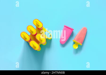 Hausgemachte Fruchtknöchel. Natürliches Erdbeereis in hellen Plastikformen auf blauem Hintergrund mit Kopierraum. Draufsicht Flat Lay Template für Ihr. Stockfoto