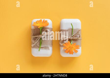 Handgemachte Naturseife, verziert mit Bastelpapier, Geißeln und orangefarbenen Ringelblumenblumen auf gelbem Hintergrund. Bio-Kosmetik-Konzept. Draufsicht F Stockfoto
