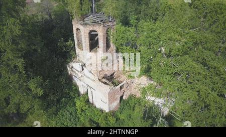 Verlassene Kirche im Wald. Luftaufnahme der alten Kirche mit einem Glockenturm und einer ruinierten Kuppel auf dem Hintergrund von grünen Bäumen in hellen sonnigen col Stockfoto