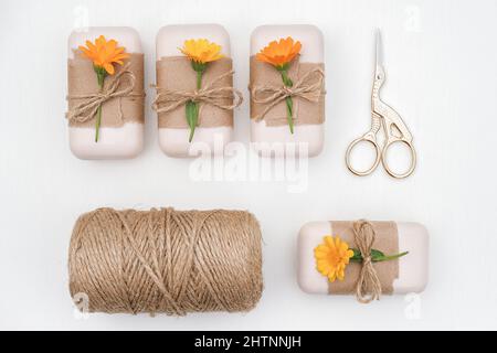 Handgemachte Naturseife mit Bastelpapier, orangen Ringelblumen, Garnklee und Schere auf weißem Hintergrund verziert. Bio-Kosmetik Co Stockfoto
