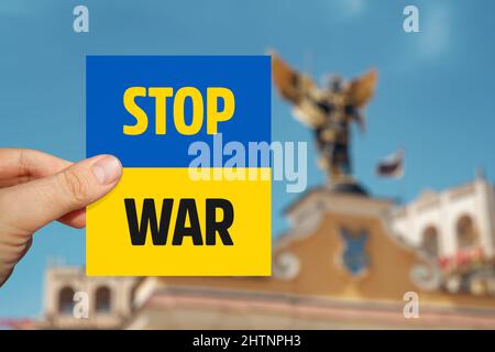 Männliche Hand mit Ukraine-Flaggenkarte und Stop war-Botschaft vor verschwommenem Kiewer Hintergrund. Stockfoto