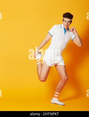 Bereit, diese Muskeln zu straffen. Ein junger Mann macht Strecken vor einem gelben Hintergrund. Stockfoto