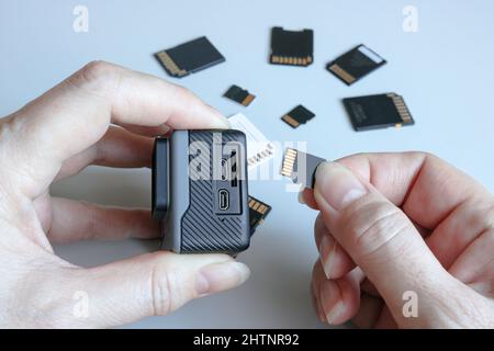 Action-Kamera und microSD-Speicherkarte in Händen auf der Rückseite anderer SD-Speicherkarten. Hintergrund von Gadgets und digitalen Geräten. Stockfoto