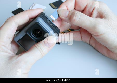 Action-Kamera und microSD-Speicherkarte in Händen auf der Rückseite anderer SD-Speicherkarten. Hintergrund von Gadgets und digitalen Geräten. Stockfoto