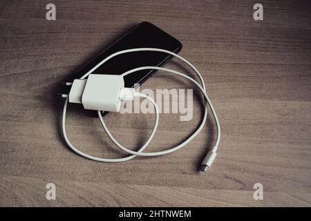 Ladegerät mit USB Typ C Kabel und Smartphone auf grunge Stil Holztisch Stockfoto