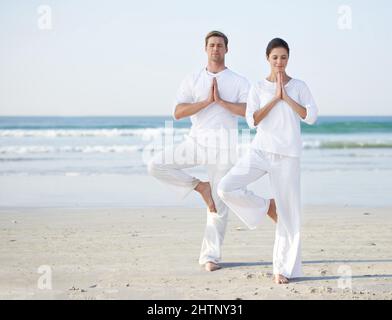 Yoga am Meer. Ein junges Paar, das am Strand Yoga praktiziert. Stockfoto