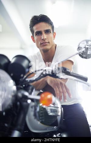 Sieht auf seinem neuen Fahrrad toll aus. Ein hübscher junger Mann, der auf seinem Motorrad sitzt. Stockfoto