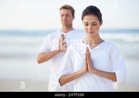 Yoga am Meer. Ein junges Paar, das am Strand Yoga praktiziert. Stockfoto