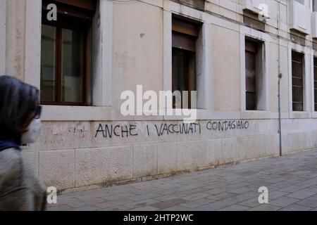 Frau mit Maske geht an Anti-Covid-Graffiti in Venedig vorbei (sogar die Geimpften sind ansteckend) Stockfoto