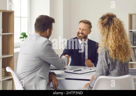 Freundlicher Anwalt, immobilienmakler oder Finanzberater schüttelt dem jungen Paar die Hände mit seinen Kunden. Stockfoto