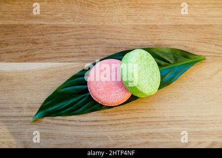 Rosa und grüne Farbe solide Shampoo-Bars oder Conditioner Bar auf grünem Blatt auf Holz Hintergrund. Minimalistisches Beauty-Set im Innenbereich, Copy Space. Stockfoto