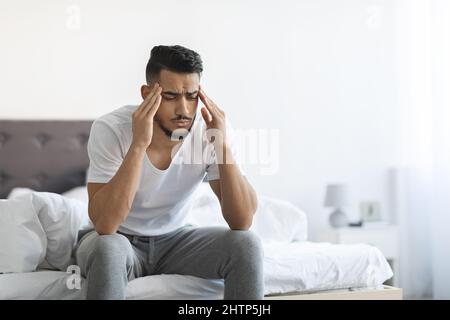 Notruf-Konzept. Porträt Eines Verärgerten Arabischen Mannes, Der Im Schlafzimmer Auf Dem Bett Sitzt Stockfoto