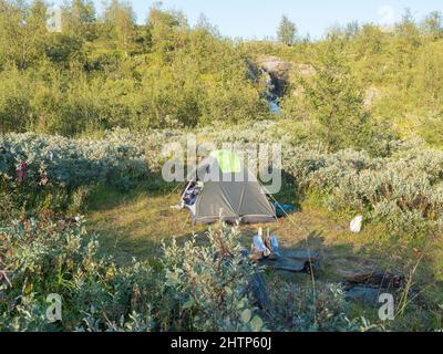 Einsames grünes Trekkingzelt in wunderschöner nördlicher Natur mit Wasserfall und Birken in der schwedisch-lappländischen Landschaft. Camping in Padjelantaleden Stockfoto