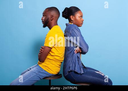 Verärgerte Menschen, die sich im Studio mit gekreuzten Armen Rücken an Rücken lehnen. Vereister Freund und Freundin mit Beziehungsproblemen und Streit vor der Kamera. Entferntes verärgertes Paar Stockfoto