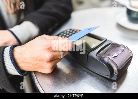 Von oben anonymen männlichen Kunden mit Kreditkarte und kontaktlosem Terminal für die Bestellung auf dem Tisch der Cafeteria zu bezahlen Stockfoto