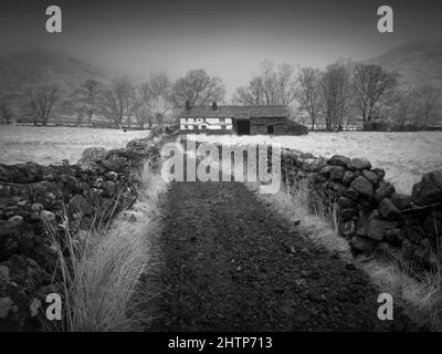 Eine Infrarotaufnahme eines rauen Tracks, der zu einer Hütte und Scheune im Little Langdale Valley, Lake District National Park, Cumbria, England führt. Stockfoto