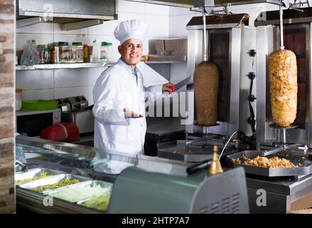 Mann Koch in Uniform schneiden Fleisch für Kebab in der Küche in Fast-Food-Restaurant Stockfoto