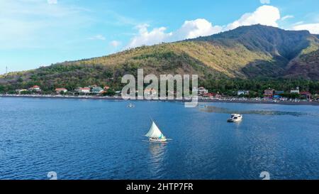 Luftaufnahme von Amed Beach in Bali, Indonesien. Traditionelle Fischerboote namens jukung am schwarzen Sandstrand und Mount Agung Vulkan in der Stockfoto