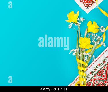 Ukrainische Urlaubskarte. Ein Strauß gelber Narzissen mit national gestickten Servietten auf blauem Hintergrund mit Kopierfläche. Blütenzusammensetzung von Th Stockfoto