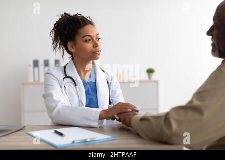 Nahaufnahme einer schwarzen Ärztin, die die Hände eines männlichen Patienten hält Stockfoto