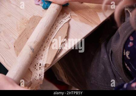 Herstellung einer durchbrochenen Tafel aus Ton mit einer gestrickten Serviette und einem hölzernen Nudelholz Stockfoto