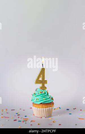 Hausgemachter Cupcake mit bunten Streuseln und einer Kerze in Form der Nummer vier auf weißem Hintergrund. Stockfoto