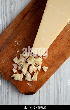 Ein Stück Parmigiano Reggiano auf einem rustikalen Holzbrett auf einem weißen Holztisch, Draufsicht. Flach liegend, über Kopf, von oben. Stockfoto