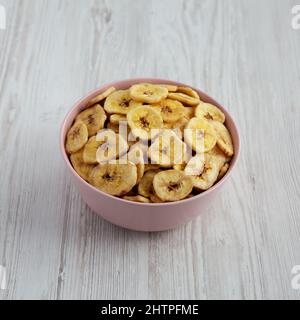 Hausgemachte Bananenchips in einer rosa Schale auf weißem Holzhintergrund, Seitenansicht. Stockfoto