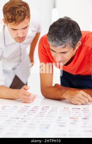 Fotos werden ausgecheckt. Zwei professionelle Fotografen, die sich Fotos auf dem Tisch ansehen. Stockfoto