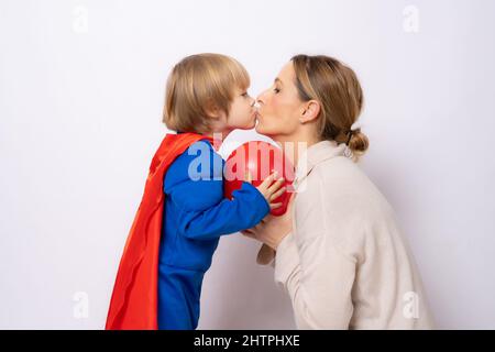 Kind Junge in Superman-Outfit küssen seine Mutter isoliert auf weißem Hintergrund gekleidet. Mutterschaft Konzept. Stockfoto